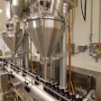 TWO FILLERS. Bottles on the conveyor line pass underneath the two Spee-Dee fillers. After the bottles are filled they are sealed and prepped for shipping.