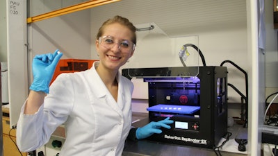 Katazyna Pietrzak, a student in Alhnan research team holding a 3D printed theophylline tablet made of 100% pharmaceutical-grade materials.