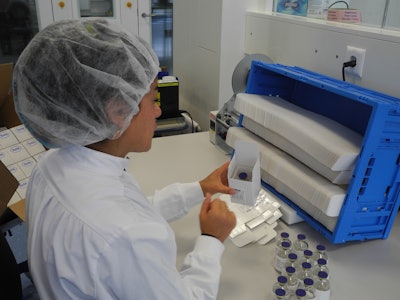 MANUAL PACKING. An operator places a glass vial into the clinical trials carton.
