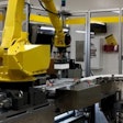 Fanuc robotic arm presenting camera with bottles.