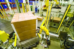 Figure 4: This end-of-line photo shows robots adding corner boards prior to stretch wrapping a load of pharmaceutical products. This system was part of an overall case packing and palletizing turnkey solution. The robots are working in a caged cell to ensure worker safety.