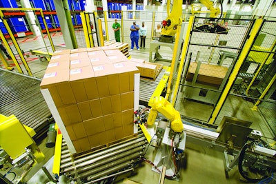 Figure 4: This end-of-line photo shows robots adding corner boards prior to stretch wrapping a load of pharmaceutical products. This system was part of an overall case packing and palletizing turnkey solution. The robots are working in a caged cell to ensure worker safety.
