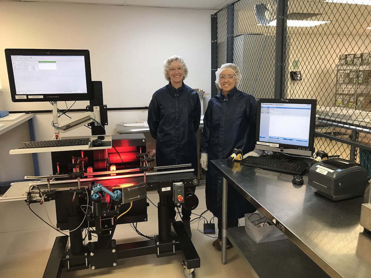 Afton Scientific&rsquo;s Kari Moore (left) and Ashley Umberger stand beside the packaging line where the serialization equipment is seen on the conveyor, with the aggregation equipment on the tabletop.