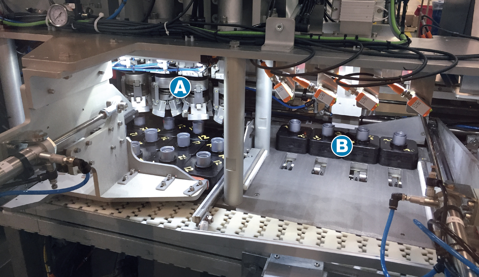 Closure Subassemblies&mdash;each in a puck and each already filled with liquid amplifier&mdash;enter the Nuspark system and are immediately pushed from a white conveyor belt and into a station where four mechanical grippers (A in photo) orient them four at a time. The pucks are then pushed to the next position (B in photo), where four Casing Subassemblies come down from above and are placed in the four Closure Subassemblies. Then the four pucks are pushed back onto the white conveyor belt, which takes them to the next station.