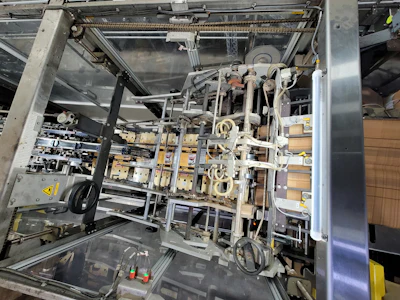 An overhead view and a side view illustrate how printed paperboard cartons are indexed out to cover, then enclose the two parallel lanes at a depth of three cans, creating the 2x3 six-pack format. No glue is required in the operation.