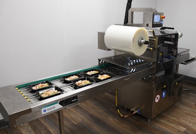 Filled trays are conveyed into the ReeEco tray-sealing machine, where film is draped over the tray, a vacuum pump removes the oxygen surrounding the product, and the film lidding is heat-sealed to the tray.