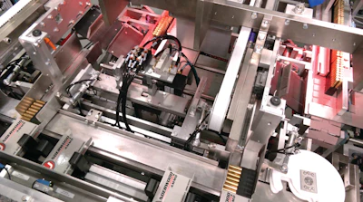 Trays of ammunition from the two-up infeed are oriented to lay on their sides before pushers load them into cartons.