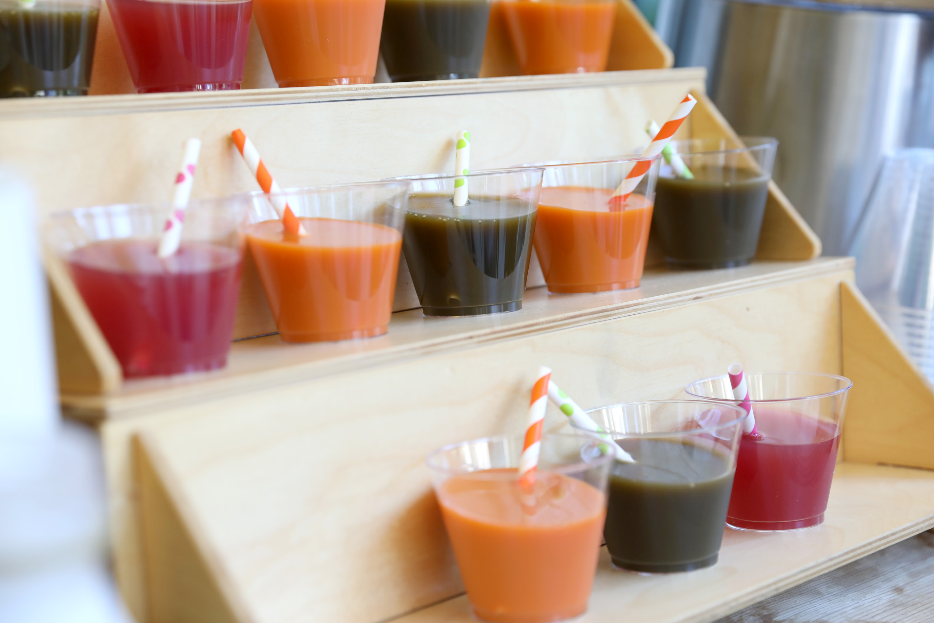 Colorful juice samples with striped straws arranged on wooden display tray