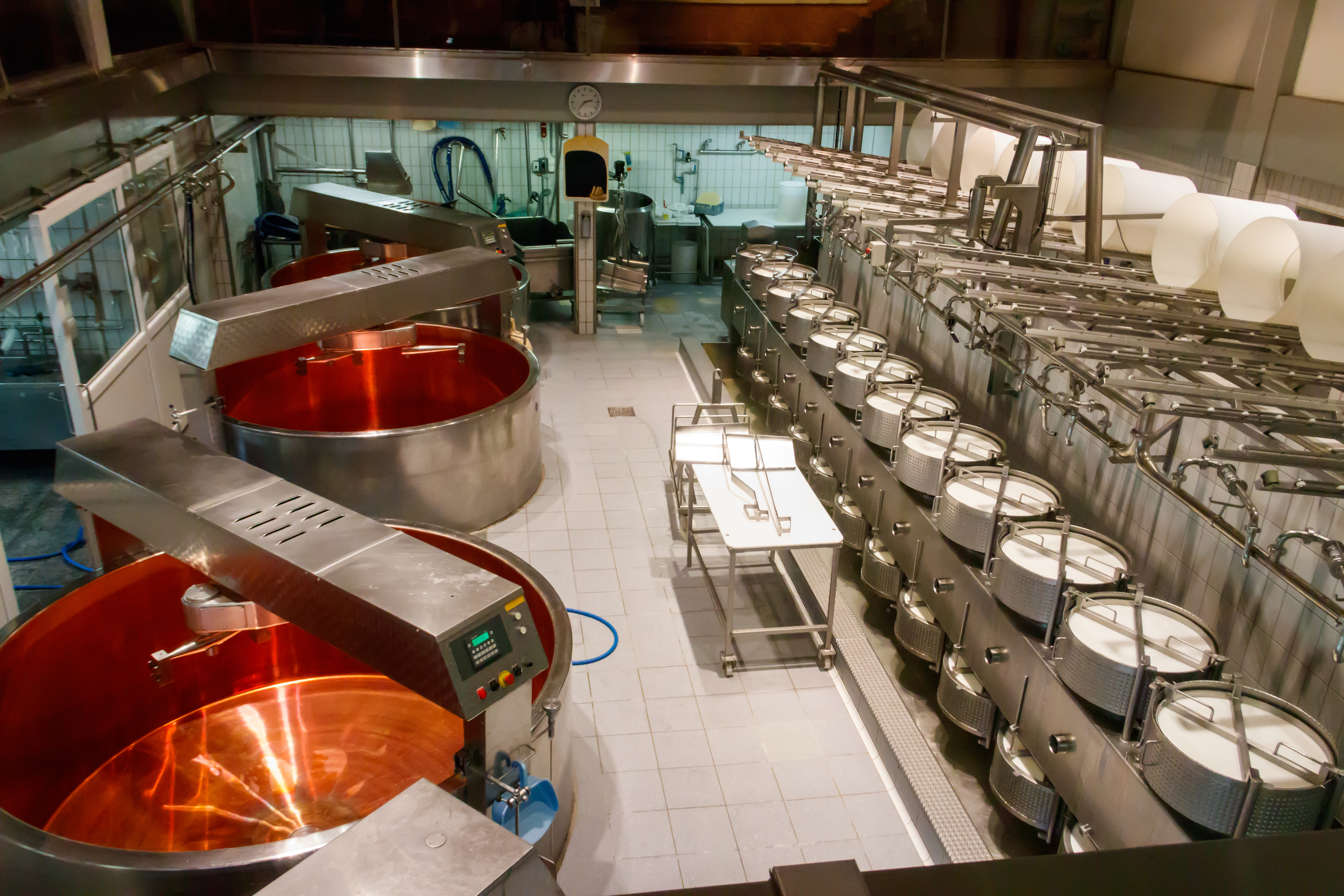 Industrial kitchen with large red mixing bowls and rows of stainless steel processing tanks