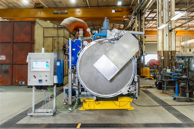 Large industrial autoclave or pressure vessel with control panel in manufacturing facility