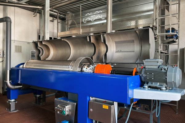 Blue industrial centrifuge machine with large metal cylindrical drum in factory setting