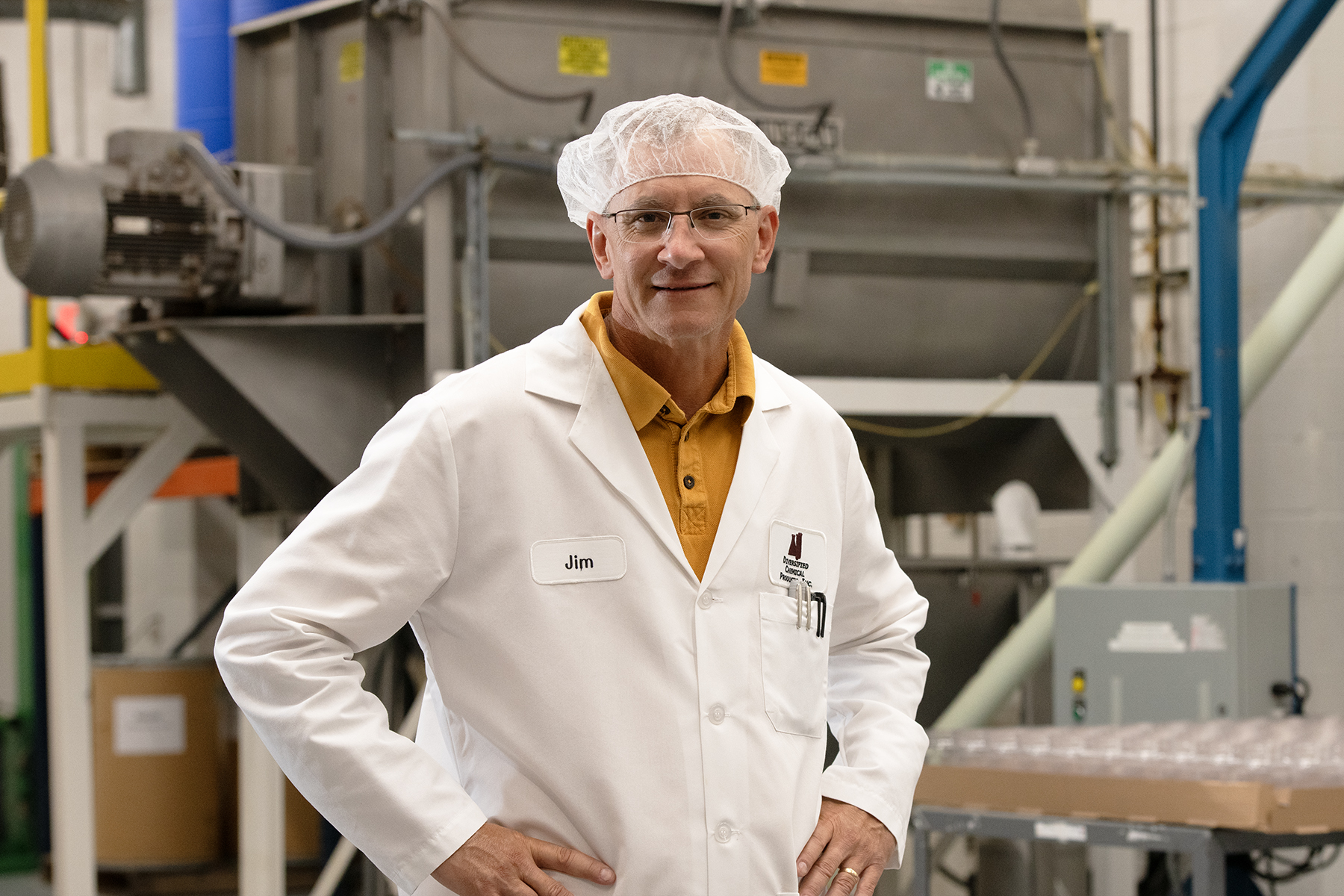 Smiling worker in white lab coat and hair net standing in food processing facility