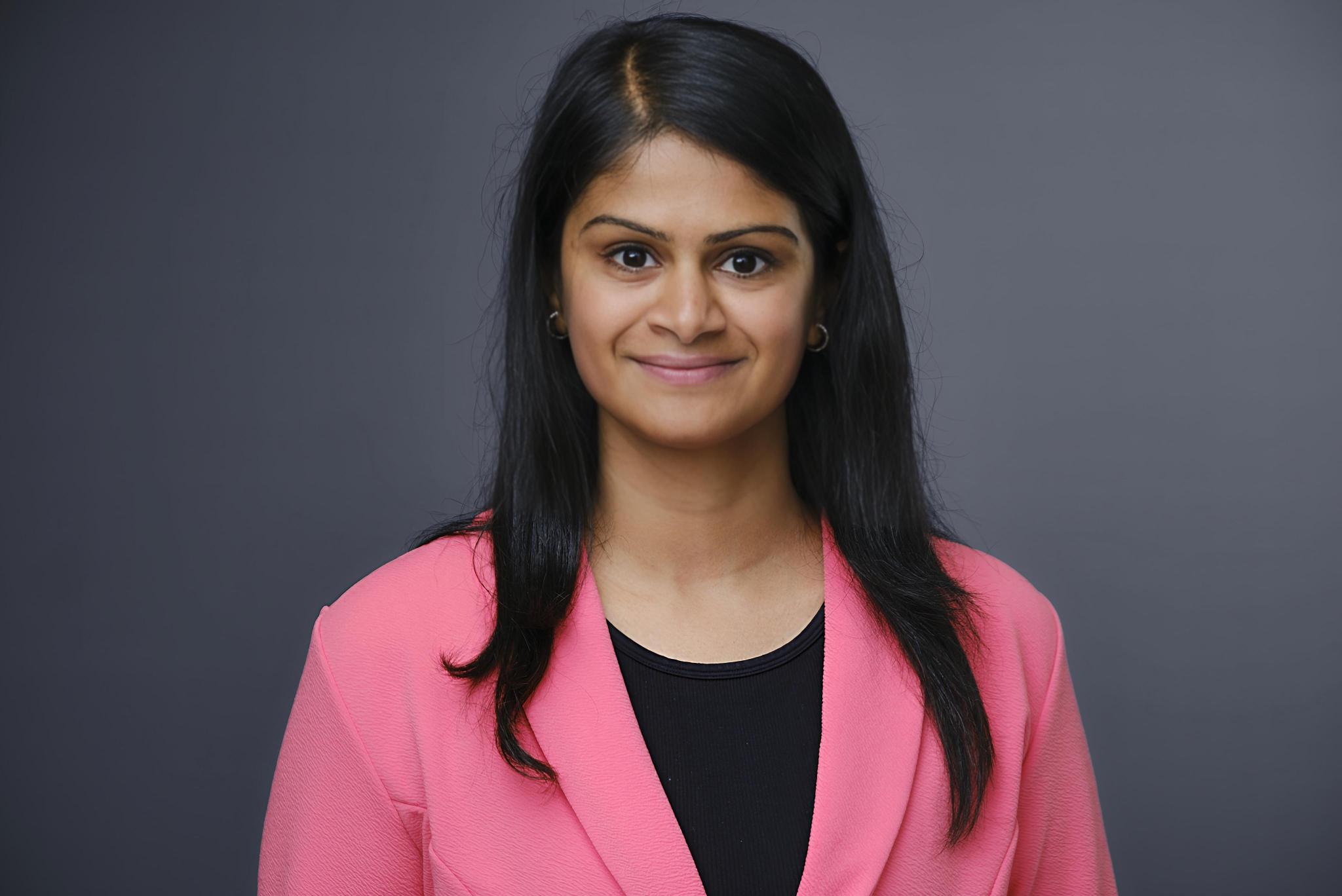 Professional woman in pink blazer smiling against gray background