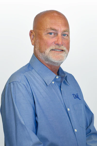Mature professional in blue button-down shirt with company logo, smiling against white background
