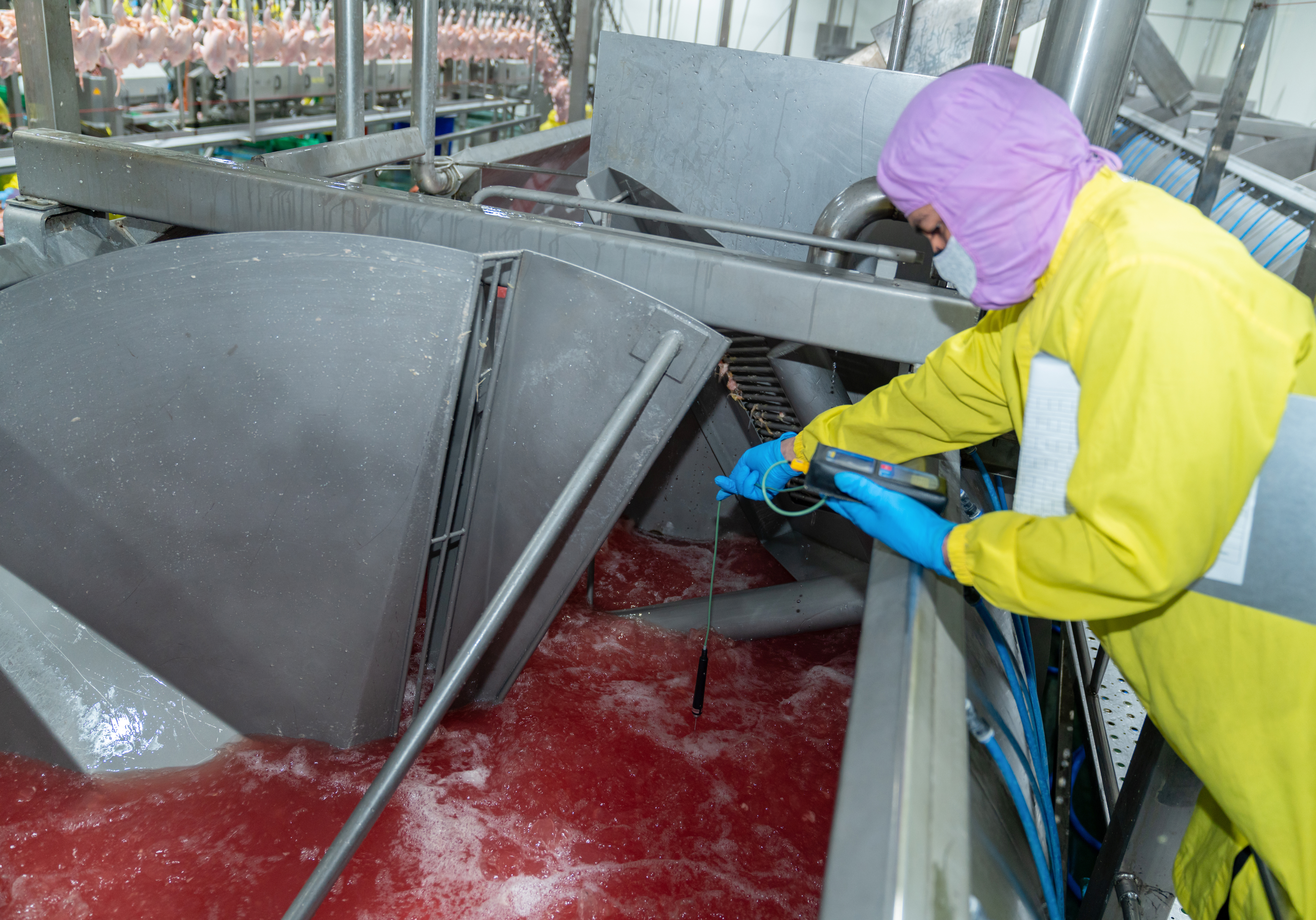 Worker in yellow protective gear cleaning red industrial food processing equipment