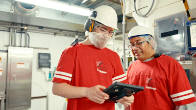 Two factory workers in safety gear review digital tablet in industrial kitchen