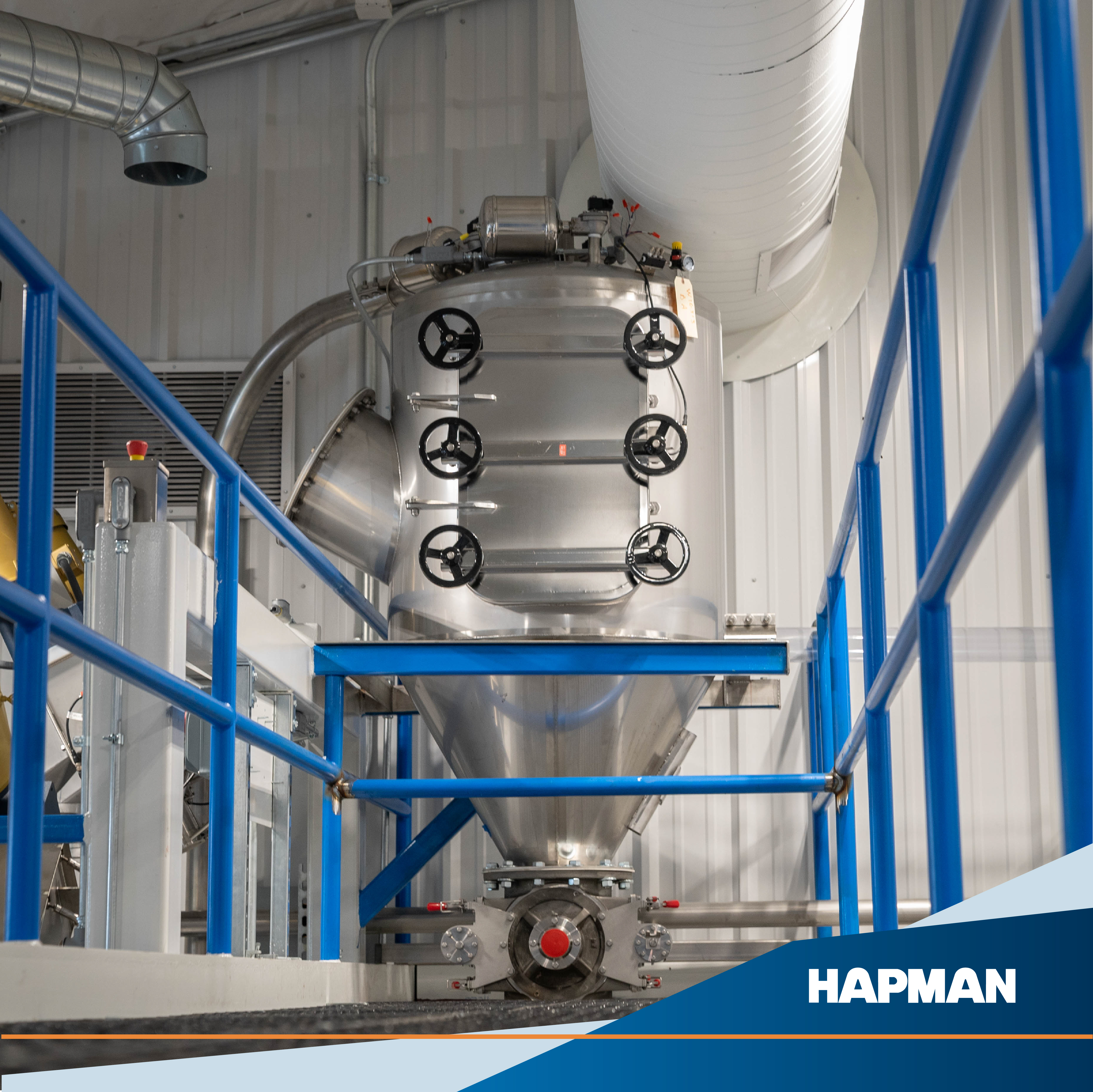 Large industrial stainless steel processing vessel with blue safety railings