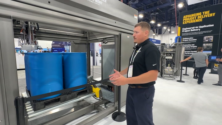 Industrial machinery technician demonstrating blue barrel handling equipment at trade show