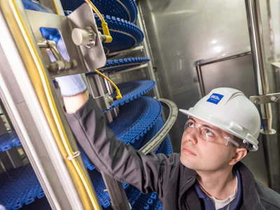 Technician in safety gear inspecting industrial machinery with blue conveyor system