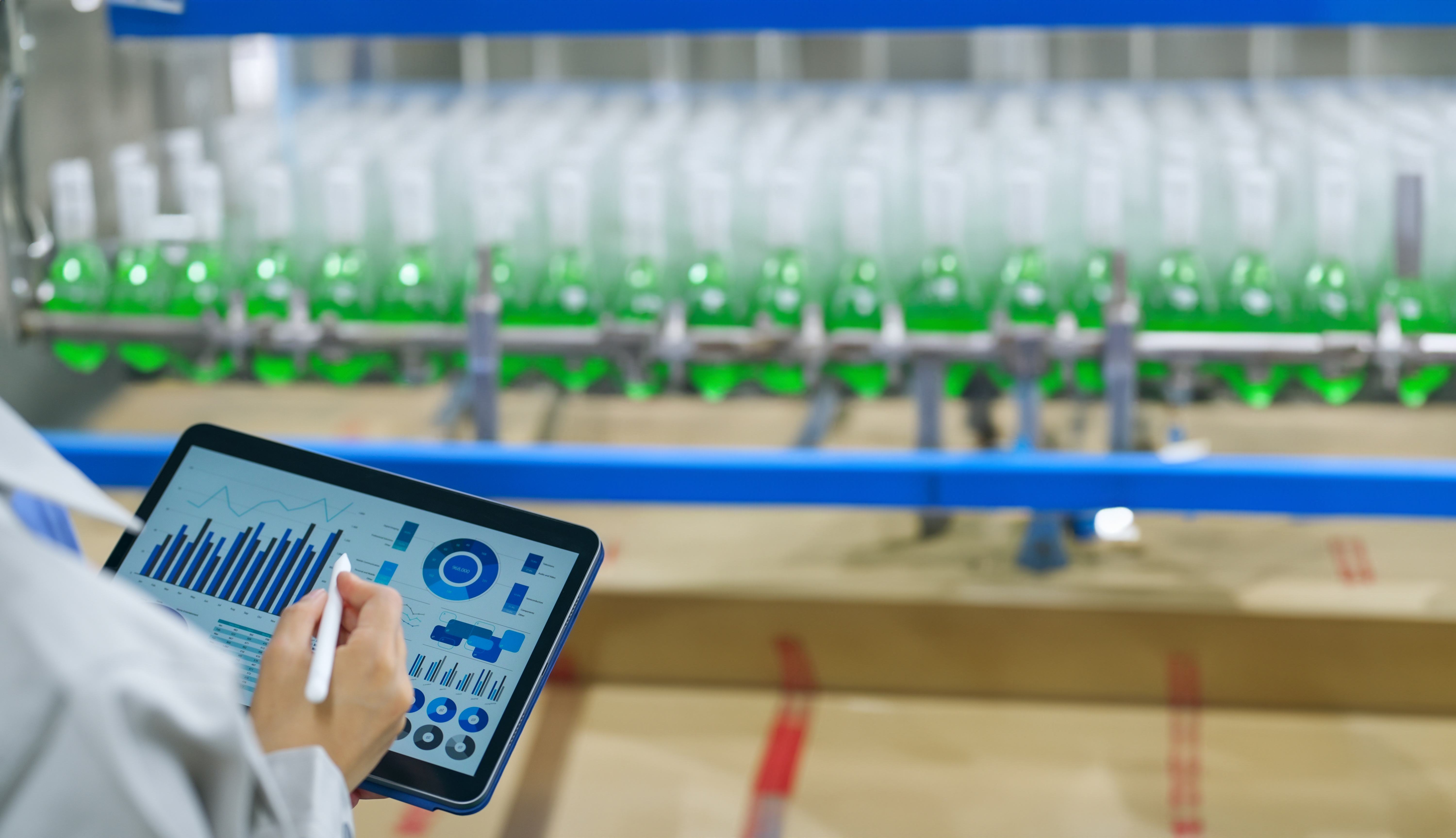 Tablet displaying analytics dashboard near industrial green bottling production line