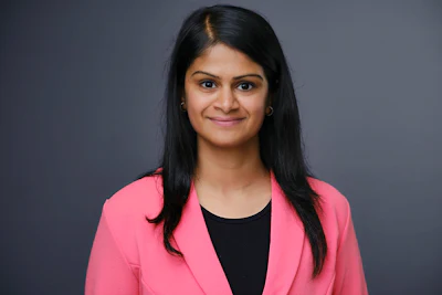 Professional woman in pink blazer smiling against gray background