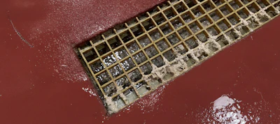 Metal drain grate with textured edges on reddish-brown surface