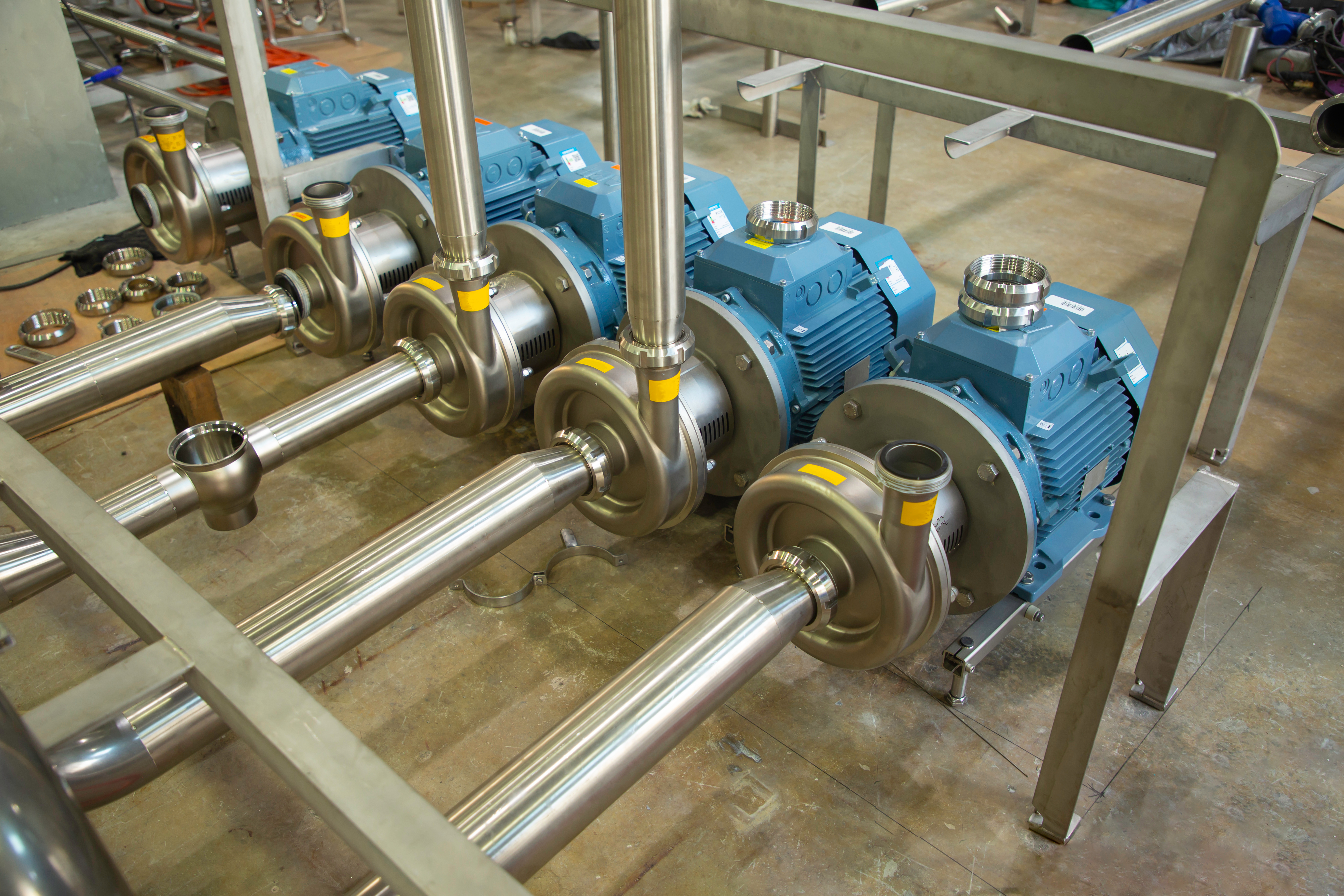 Industrial pump system with blue electric motors and stainless steel shafts mounted on metal frame in factory
