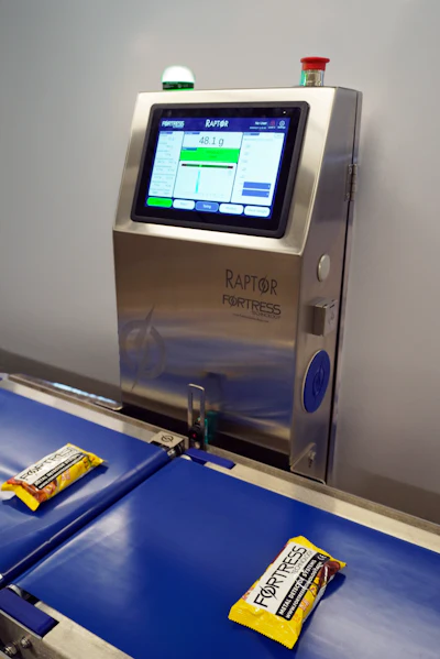 Raptor Fortress industrial weighing scale displaying 49.1g with packaged food items on blue conveyor platform