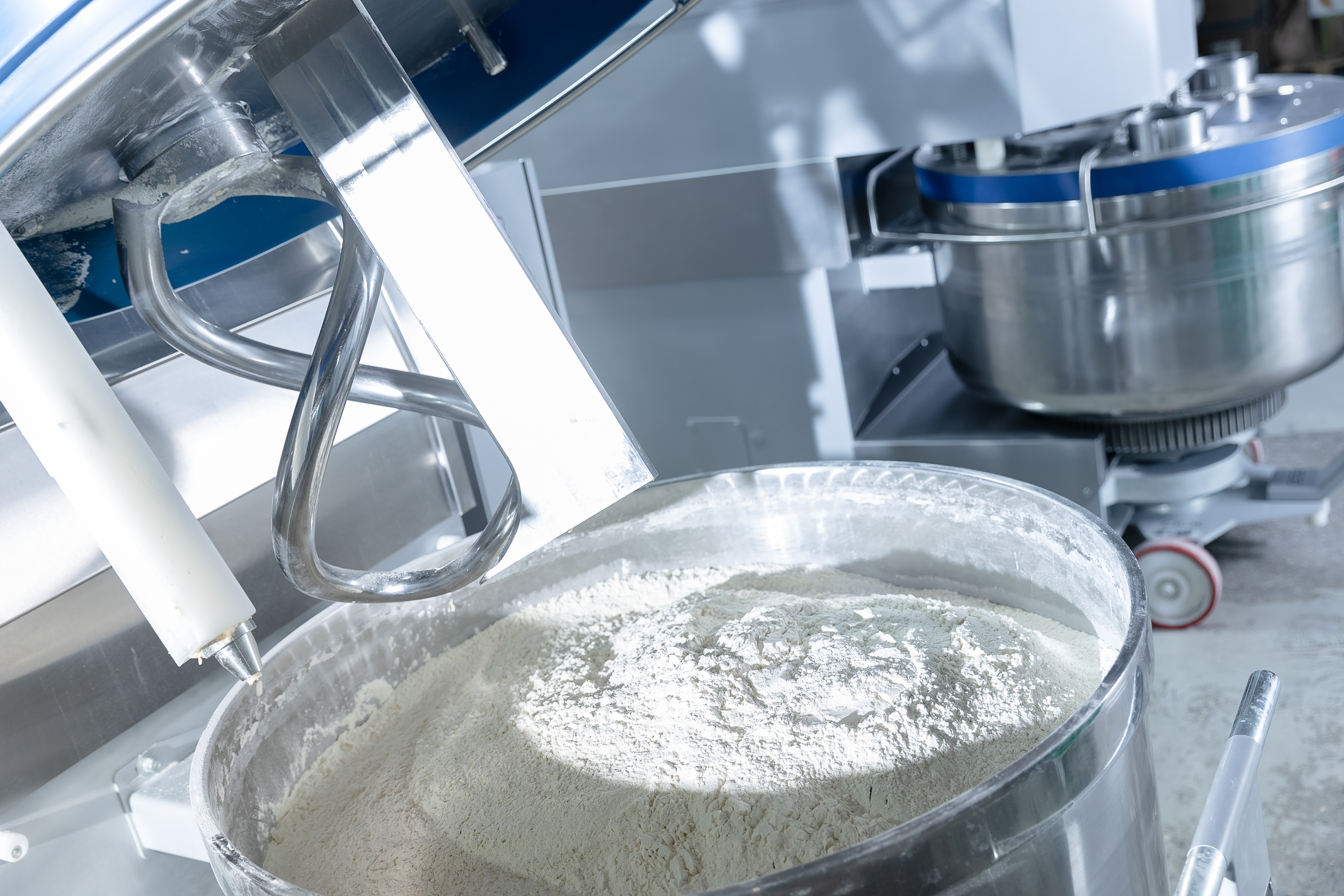 Stand mixer with bowl of flour and stainless steel mixing bowls on kitchen counter