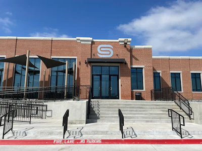 Modern brick building with white 'S' logo and concrete steps with metal railings