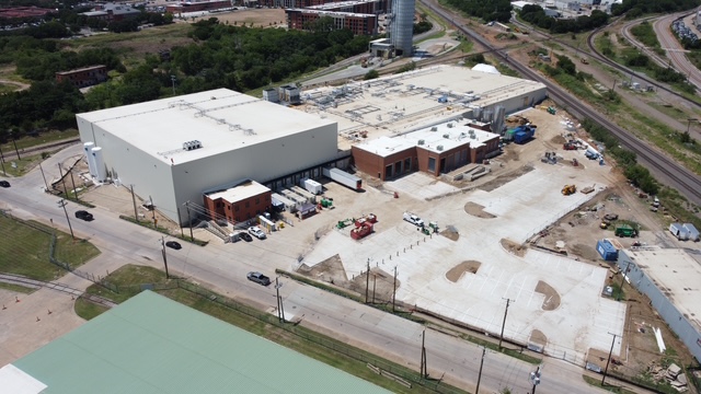 Aerial view of industrial warehouse complex under construction with white roof, surrounding buildings, and equipment on site