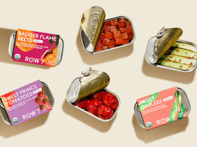 Row 7’s tinned vegetables are packed in small-format tins with paperboard sleeves that leave the container visible, reinforcing the brand’s produce-aisle positioning and connection to fresh, flavor-bred vegetables.