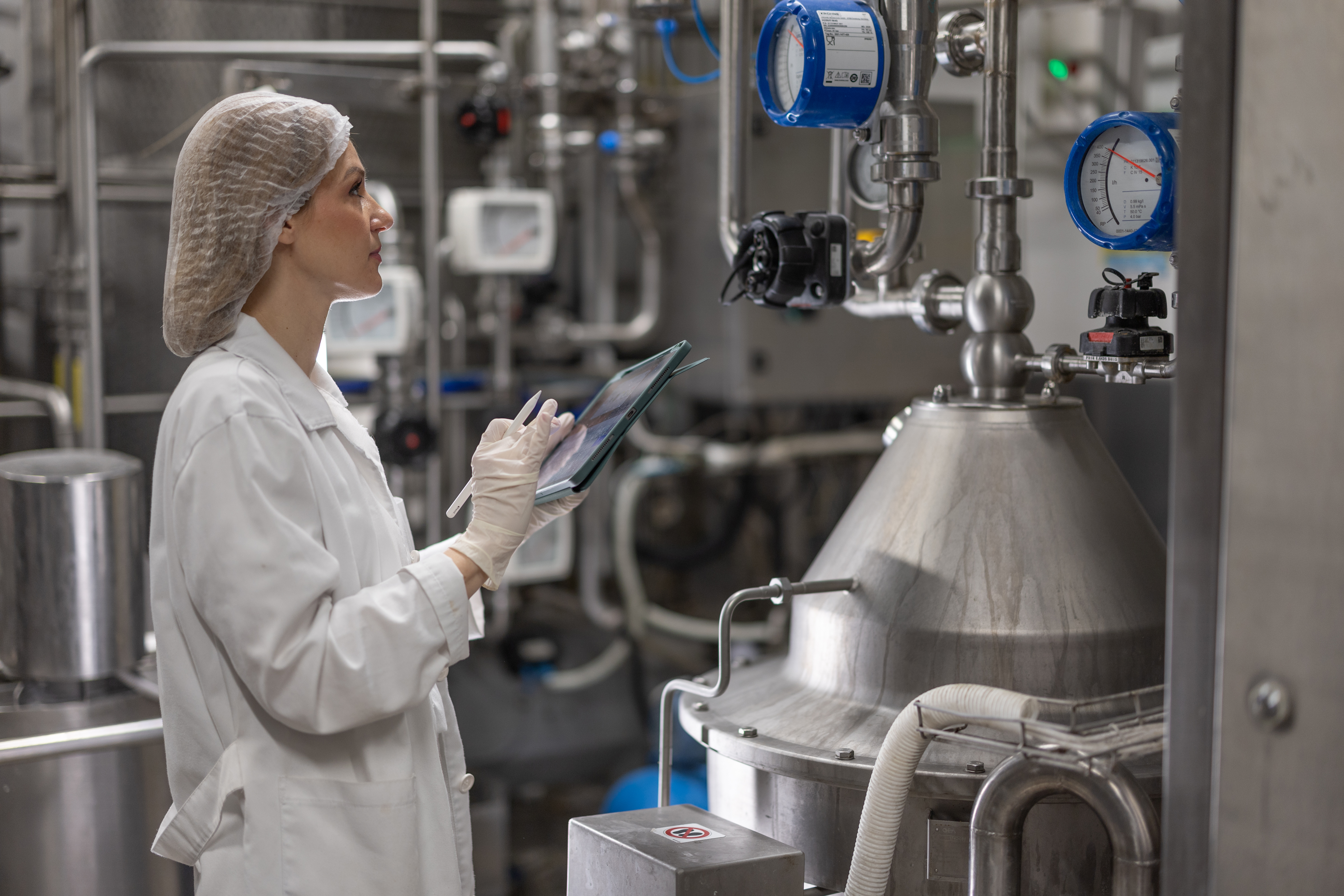 Pharmaceutical technician in cleanroom monitoring stainless steel bioreactor equipment with pressure gauges and piping