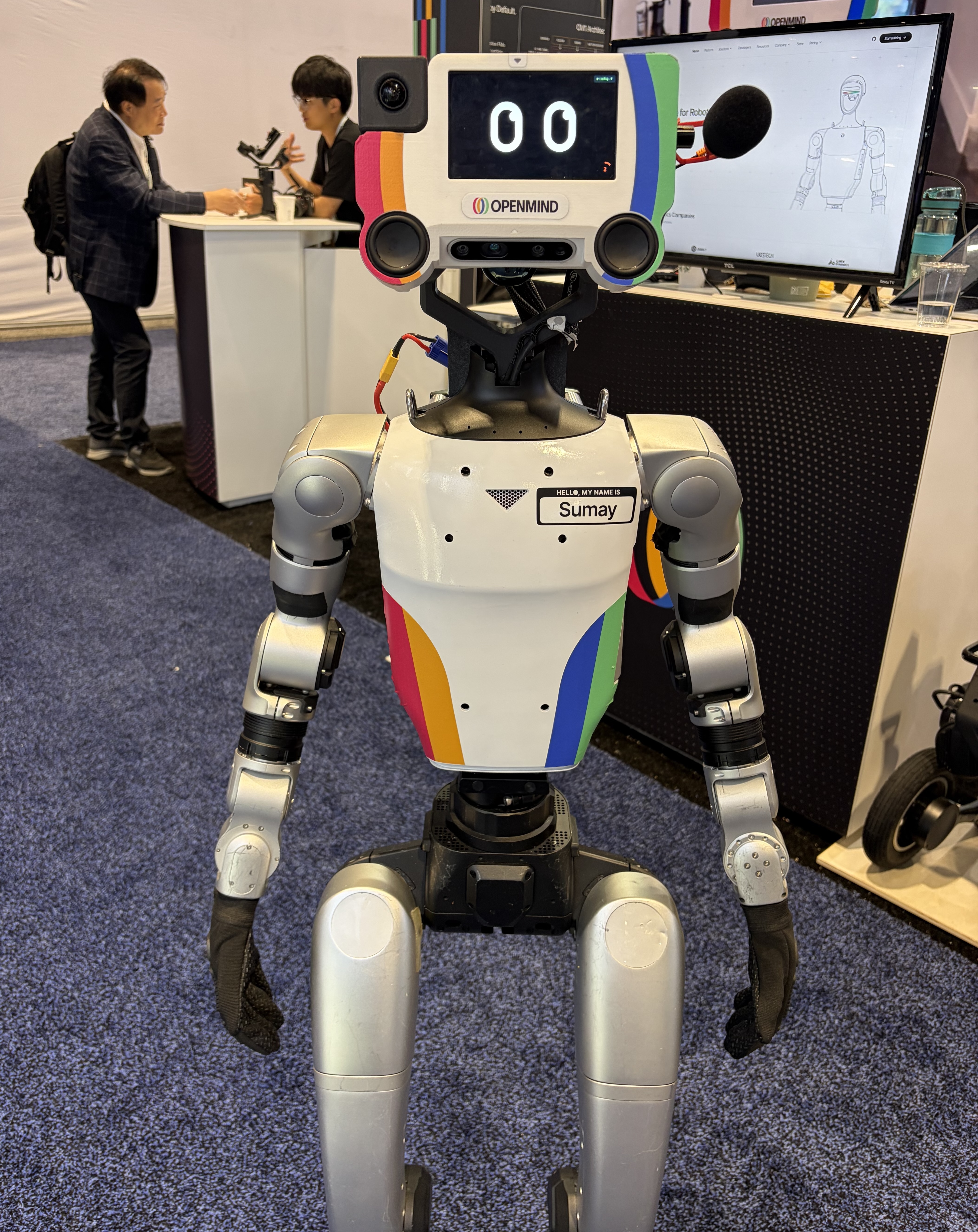 Sumay, a humanoid powered by OpenMind's software, draws a crowd at Automate 2026's Humanoid Robot Pavilion. The engineering impresses, but bipedal humanoids remain a few cycles away from the packaging floor.