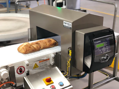 Industrial bread slicer with baguette on conveyor belt in commercial kitchen facility