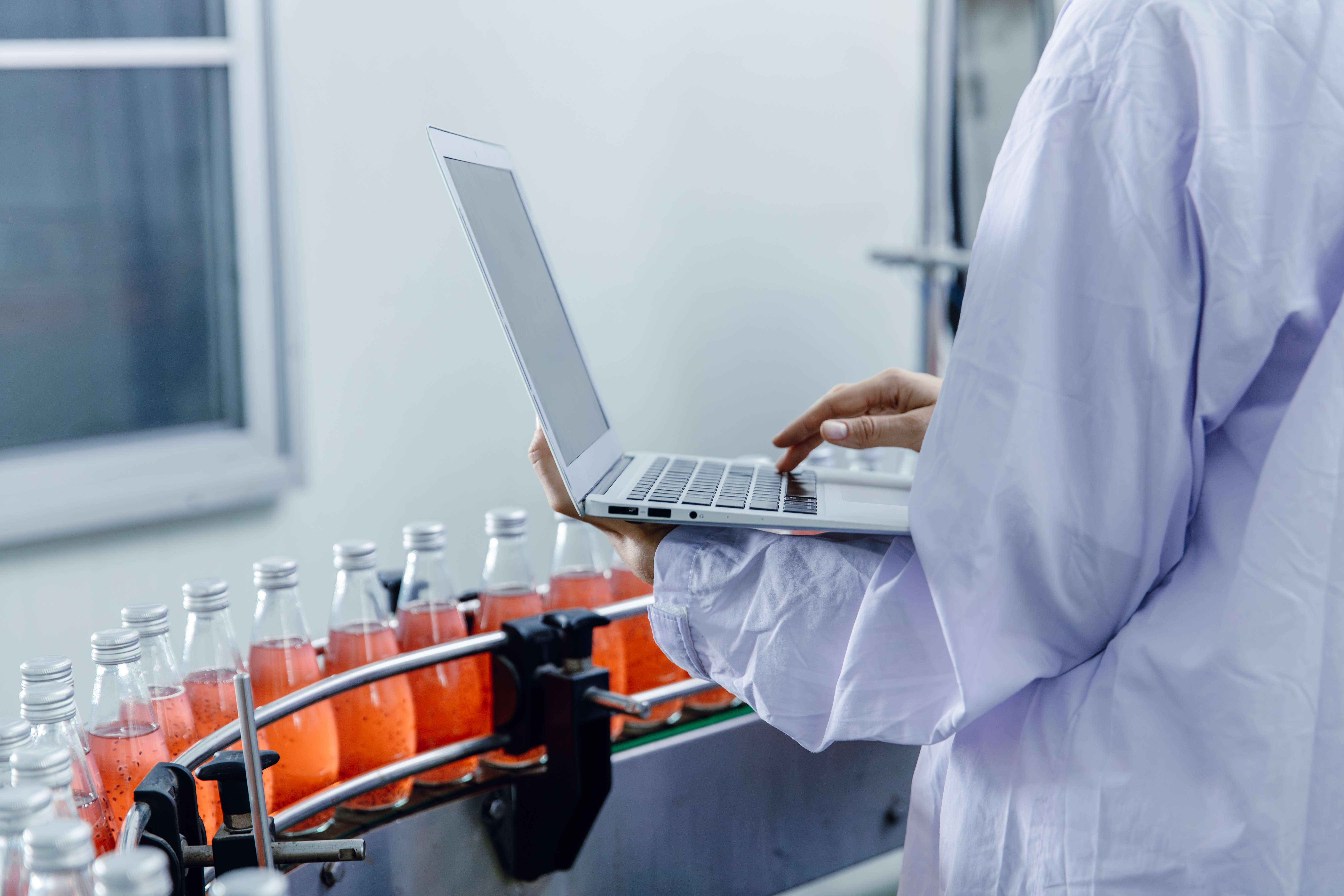 Scientist in lab coat using laptop while monitoring red liquid samples in glass vials on laboratory equipment