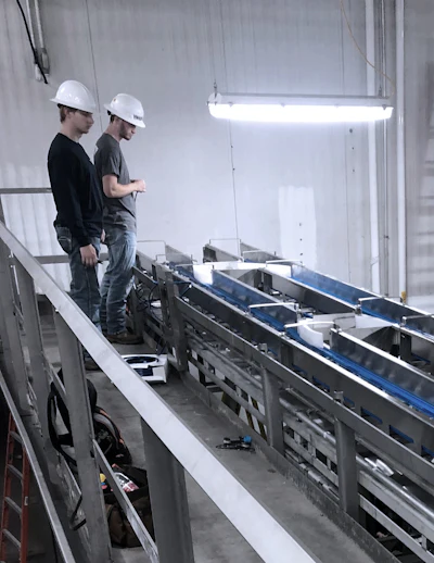 Two construction workers in hard hats inspecting industrial machinery in a warehouse with overhead lighting
