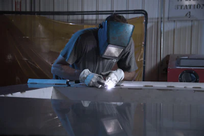 Welder in protective gear performing arc welding on metal surface in industrial workshop