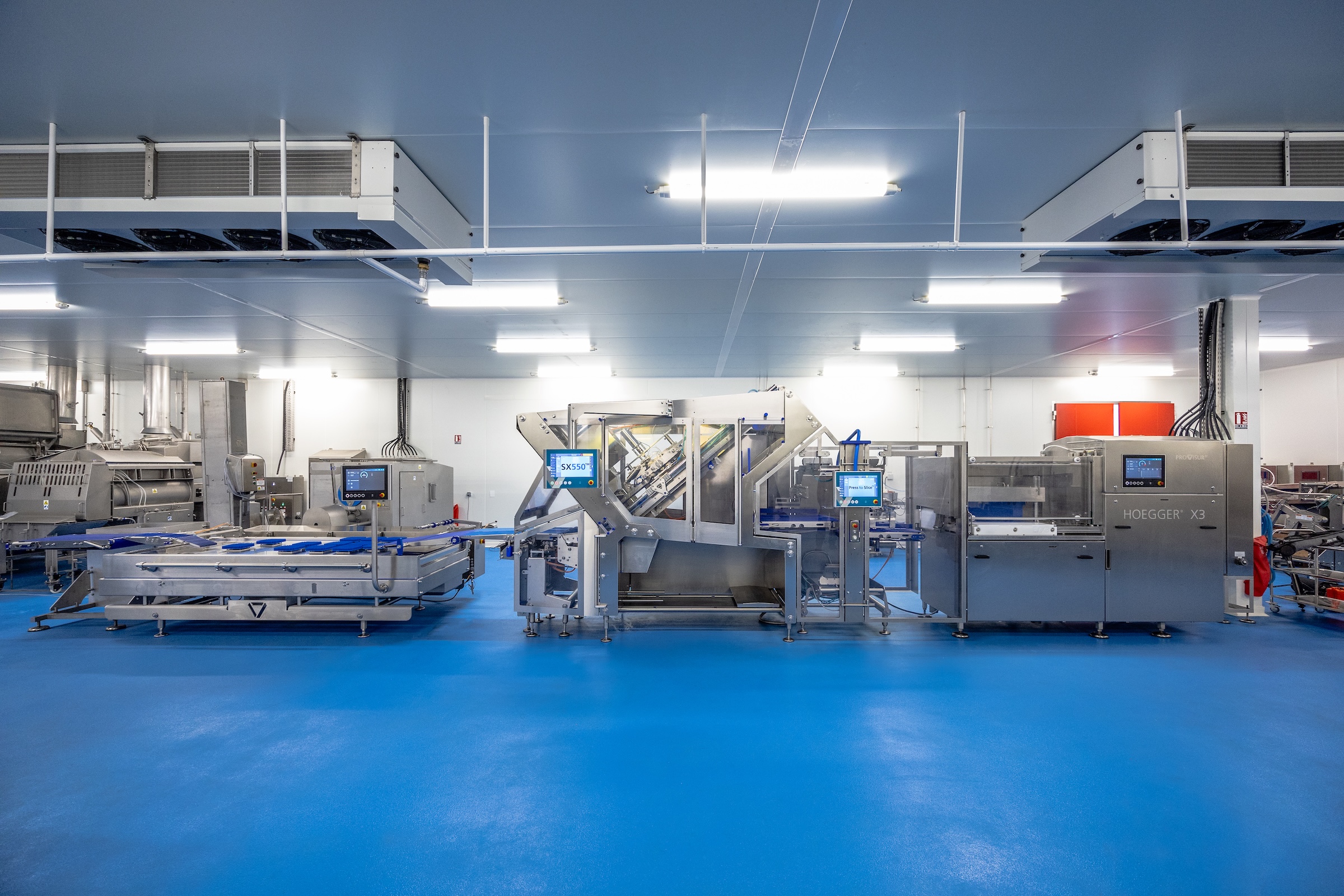 Industrial food processing facility with blue flooring, automated machinery, overhead lighting, and HVAC systems