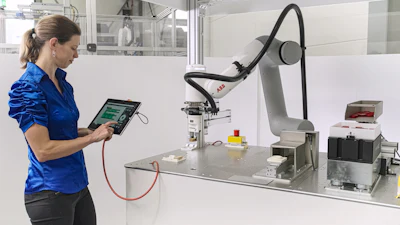 Technician operating robotic arm system with control panel in industrial laboratory setting