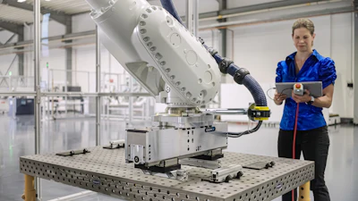 Female technician holding tablet next to industrial robotic arm in manufacturing facility