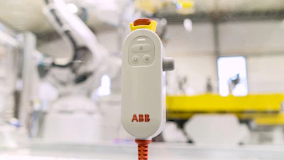 ABB remote control pendant with yellow emergency stop button in industrial robotic workspace