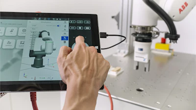 Engineer using CAD software to design robotic arm in industrial workspace with ABB robot visible