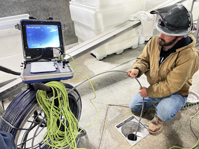 Technician performing sewer pipe inspection using camera equipment and monitoring display at ground level
