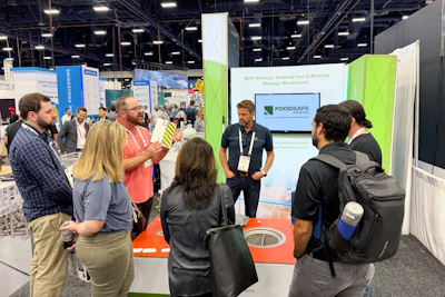 Attendees gathered at a FoodSafe Systems trade show booth featuring green and white branding and interactive displays.