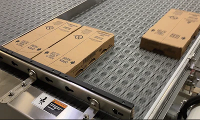 Cardboard shipping boxes on industrial conveyor belt with metal frame and gray textured surface