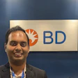 Professional man smiling at BD corporate event or office with company logo signage in background