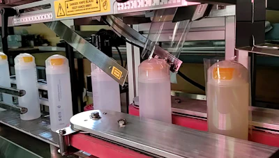3D printer setup with supply bottles and industrial equipment on red platform