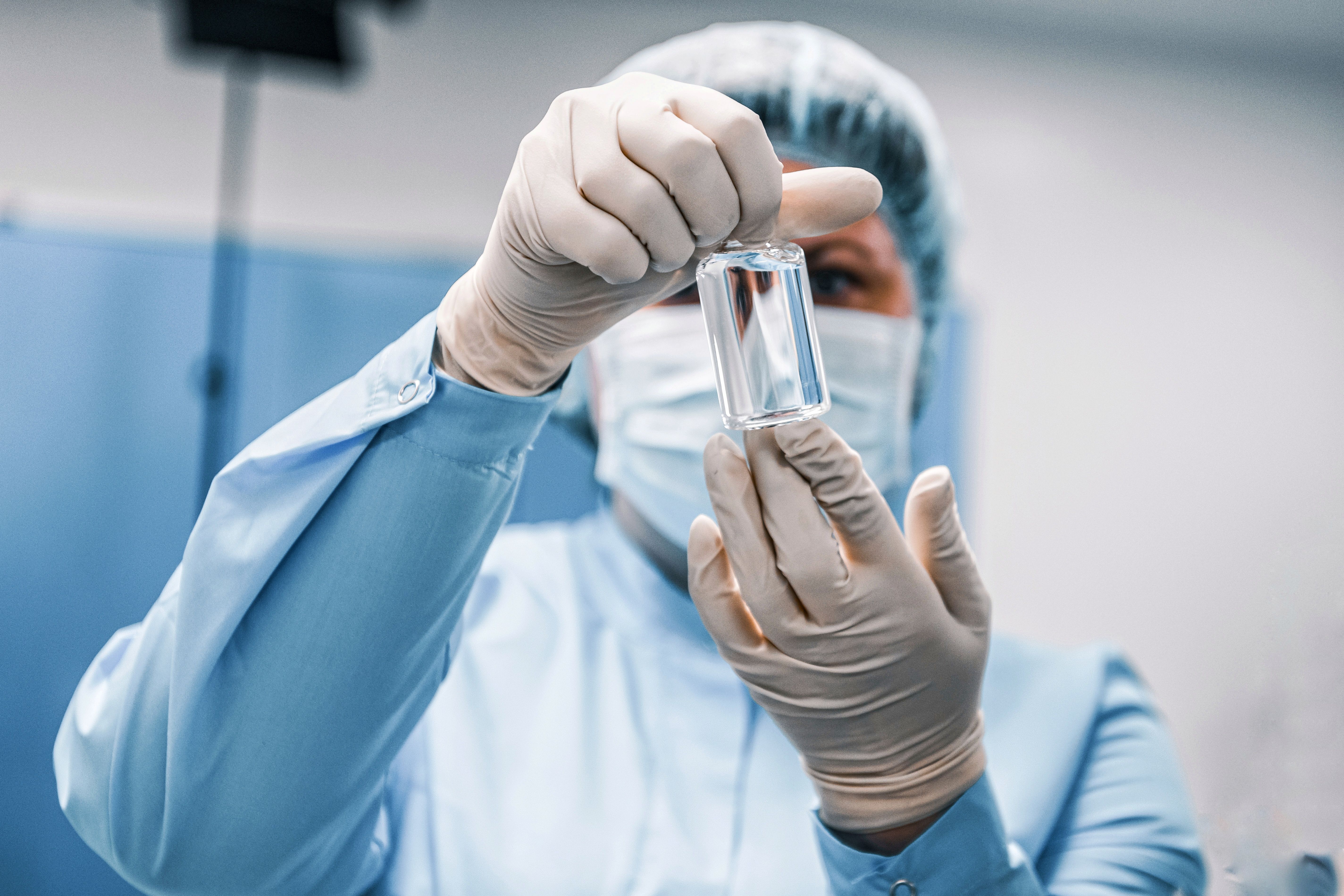 Laboratory technician in sterile protective gear holding a clear glass vial for sample analysis