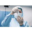 Laboratory technician in sterile protective gear holding a clear glass vial for sample analysis